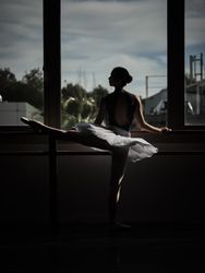 Graceful ballerina raising and stretching leg at barre at sunset