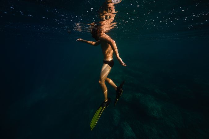Anonymous male tourist diving undersea in sunlight