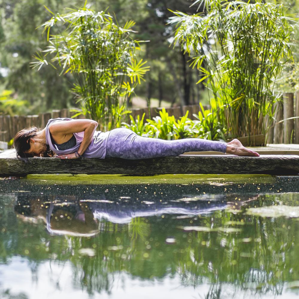 Relaxed fit woman lying on a tree trunk over the water.