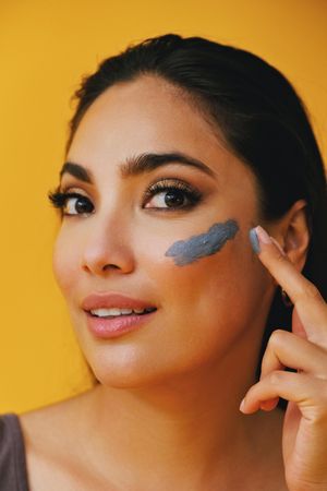 Latina woman looking at camera while applying clay mask with hand