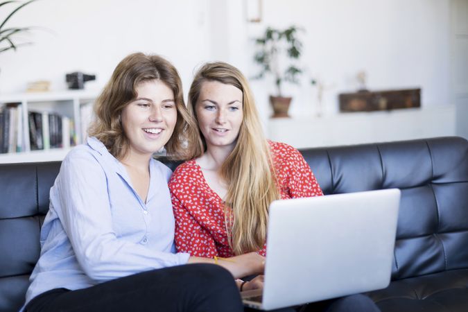 Two young women using computer while sitting on couch