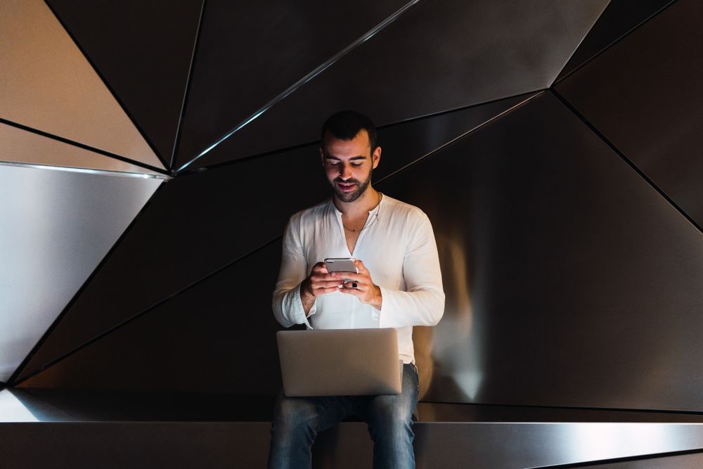 Man with laptop browsing smartphone in studio