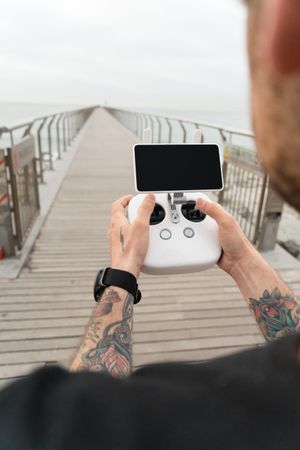 Man with remote for drone on wooden boardwalk on beach