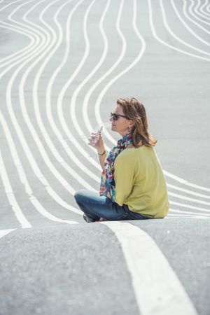 Modern relaxed woman vaping while sitting on marked road