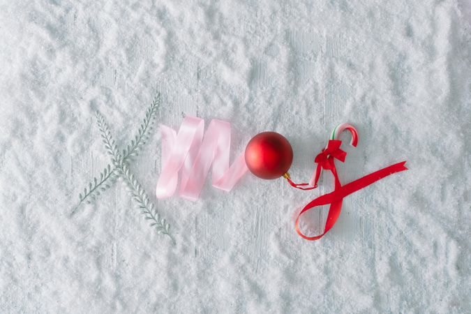 Wooden table background with “Xmas” written in ribbon, baubles, candy cane and leaves