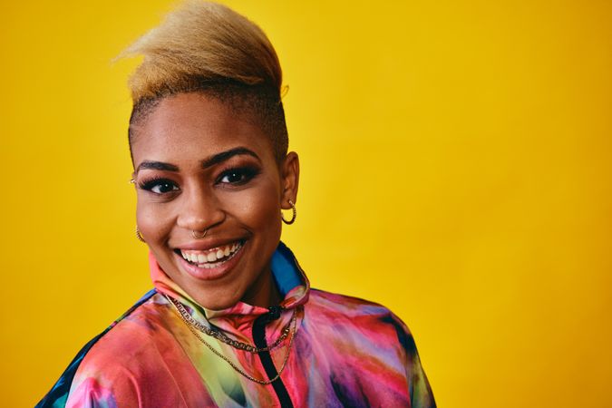 Closeup of cheerful Black female in colorful jacket against yellow background