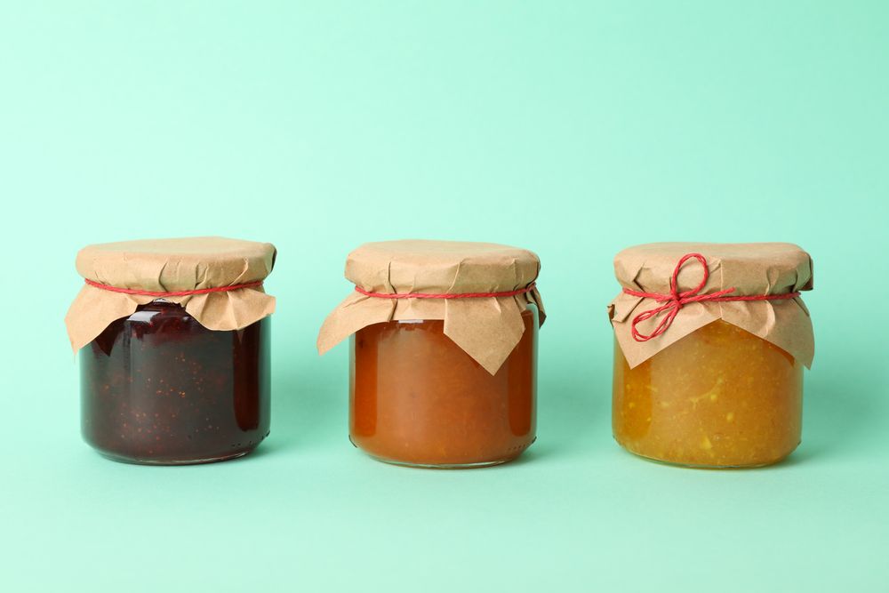 Glass jars with jam on mint background, space for text