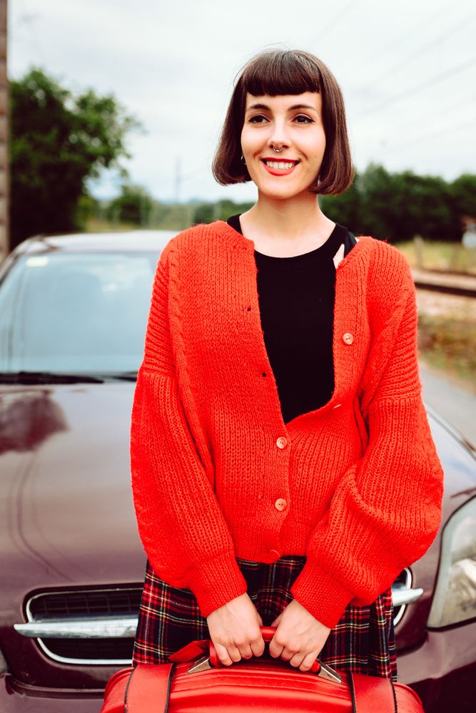 Smiling woman in red with suitcase nearby car