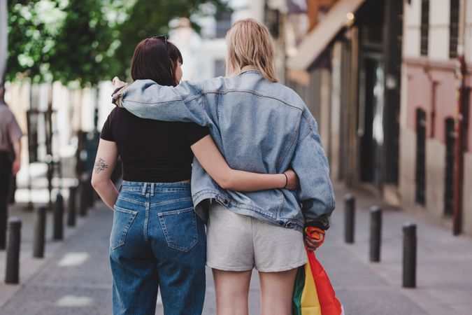 Lesbian couple with LGBT flag walking on street