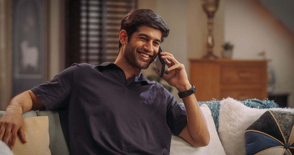 Young Indian Man Talking On The Phone At Home: Discussing Work Updates, Coordinating with Colleagues