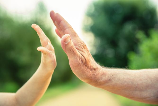 Child and older man's hands high fiving in the nature