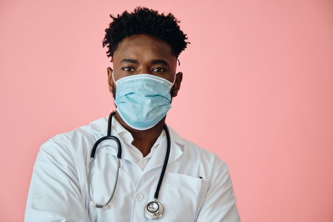 Close up portrait of Black male doctor in pink studio with stethoscope and facemask