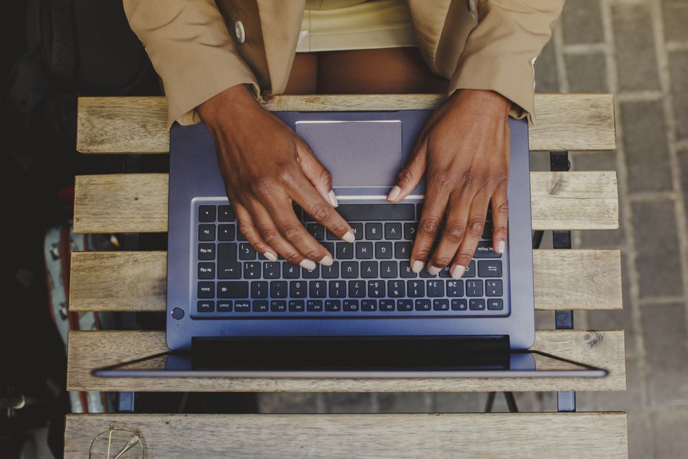 Black woman sitting at table and browsing on laptop in cafe