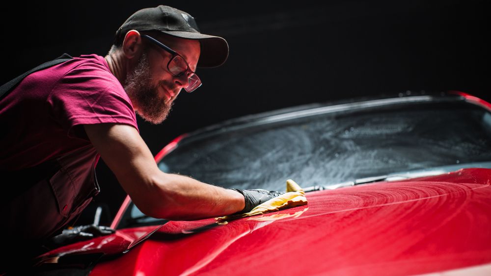 Car Wash Expert Using a Microfiber Cloth to Dry Up a Red Modern Sportscar.