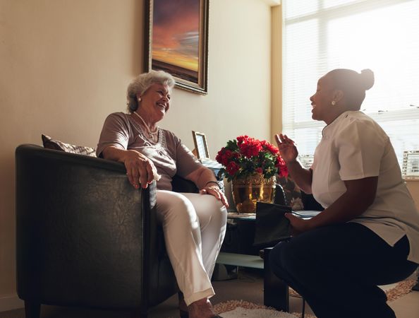 Home caregiver talking with a older woman sitting on chair at home