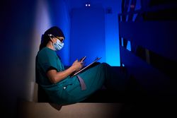 Woman in mask and scrubs sitting on stairs