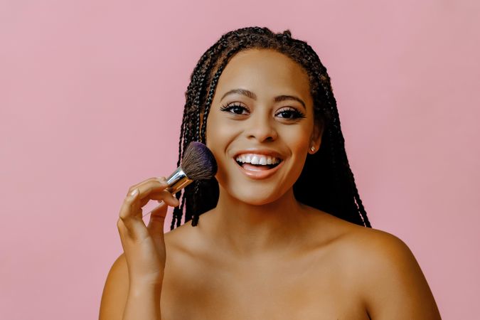 Happy Black woman holding make up brush to her cheek with eyes closed