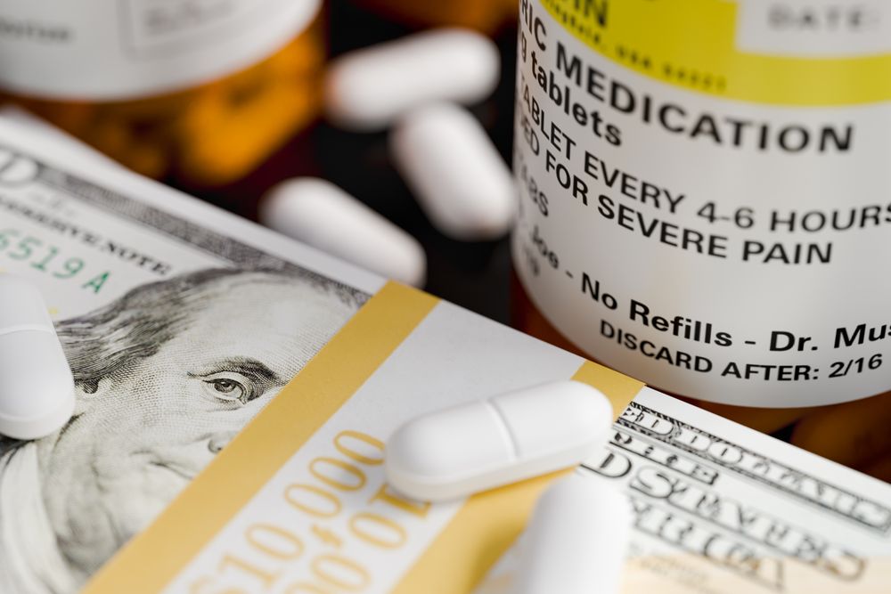 Prescription Medicine Bottles and Pills Next To Stacks of 100 Dollar Bills.