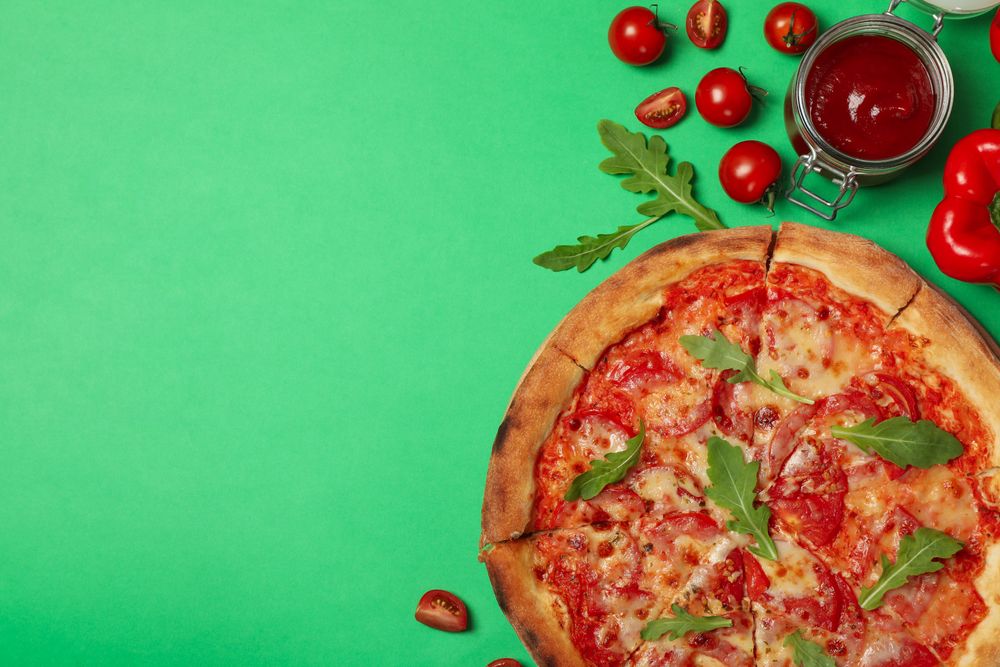 Tasty pizza and ingredients on green background