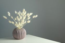 Round and ridged vase in grey room filled with dried flowers with copy space