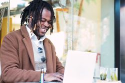 Happy Black man browsing on laptop on restaurant terrace