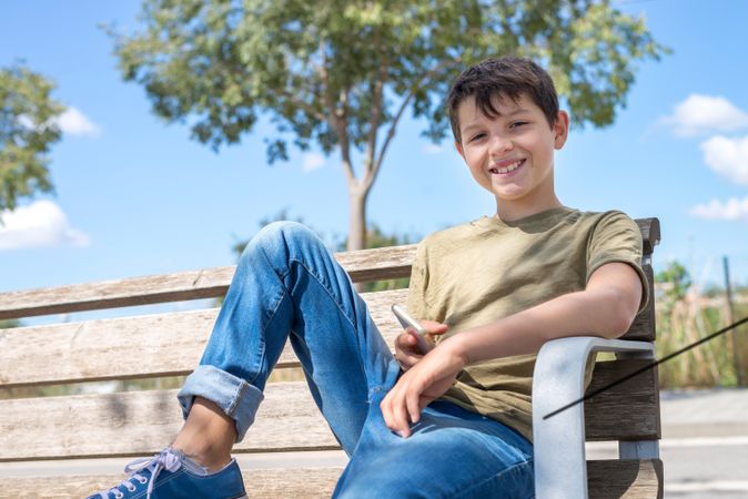 Smiling boy sitting on bench holding phone in lap