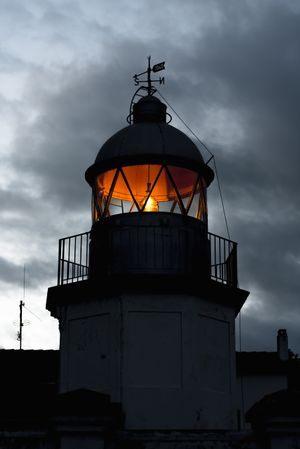 Shining lighthouse against cloudy sky