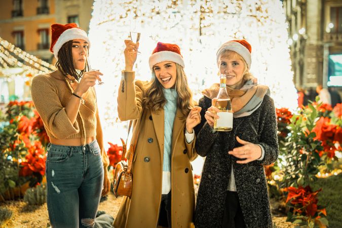 Three happy women in Santa hats toasting with champagne and looking at the camera.