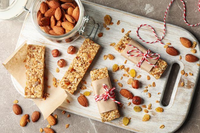 Board with tasty granola bars and nuts on gray background, top view