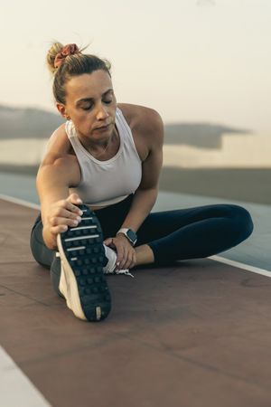 Fit woman doing a hamstring stretch on a running track after her workout