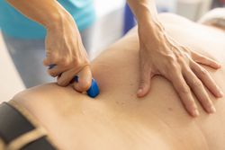 A female physiotherapist massaging the back of an older man with a massage tool