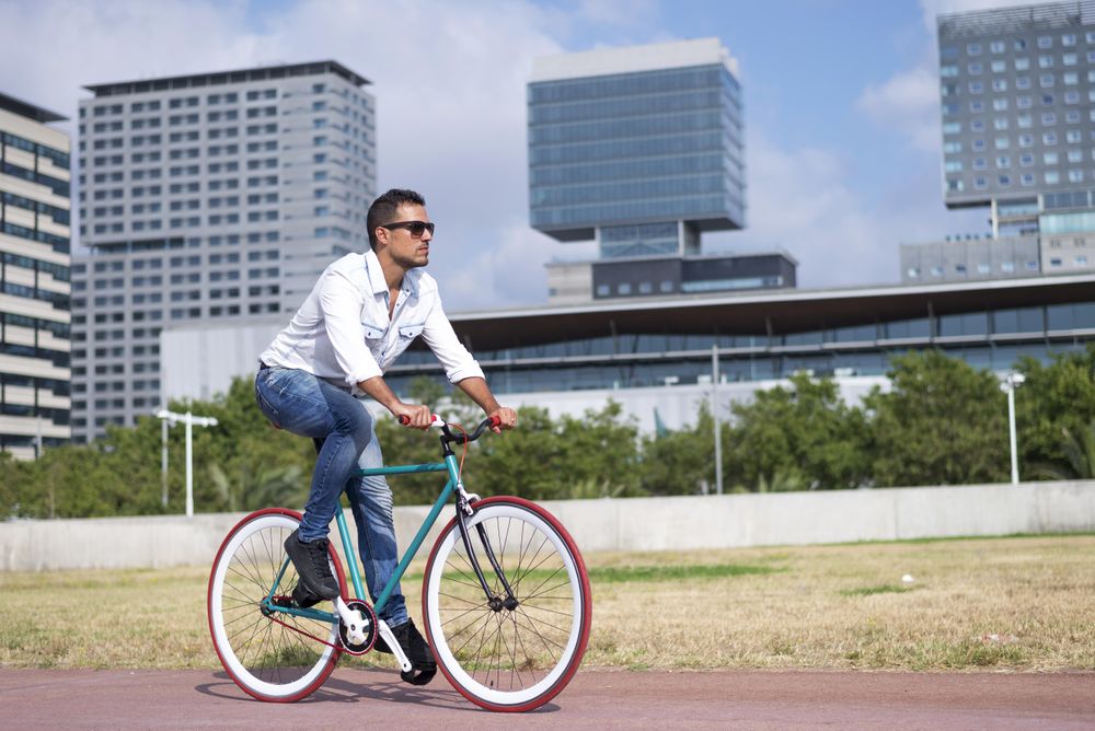 Male riding red and green bike outside next to city buildings