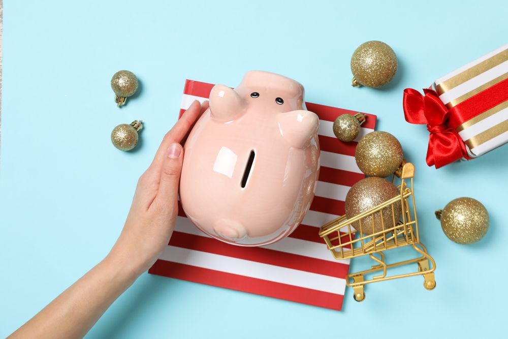 Piggy bank, female hand, gift boxes and trolley with balls on blue background, top view