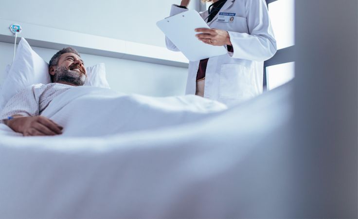 Smiling sick man lying in bed with doctor standing by