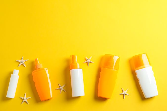 Flat lay composition with sunscreen sprays and starfishes on color background, space for text. Summer vacation backdrop
