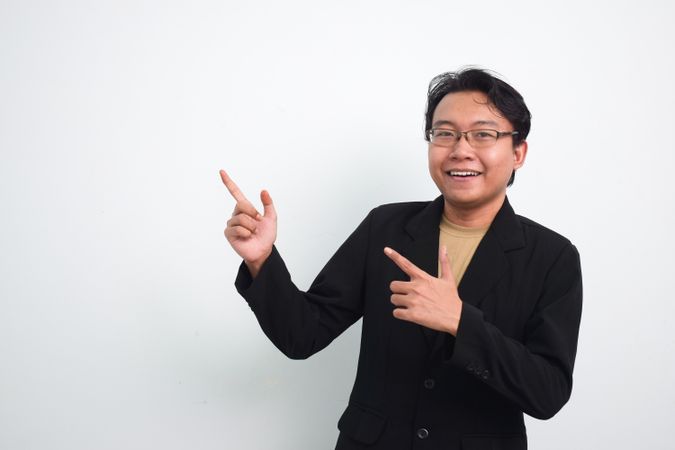 Joyful Asian businessman with suit and casual shirt pointing to the left