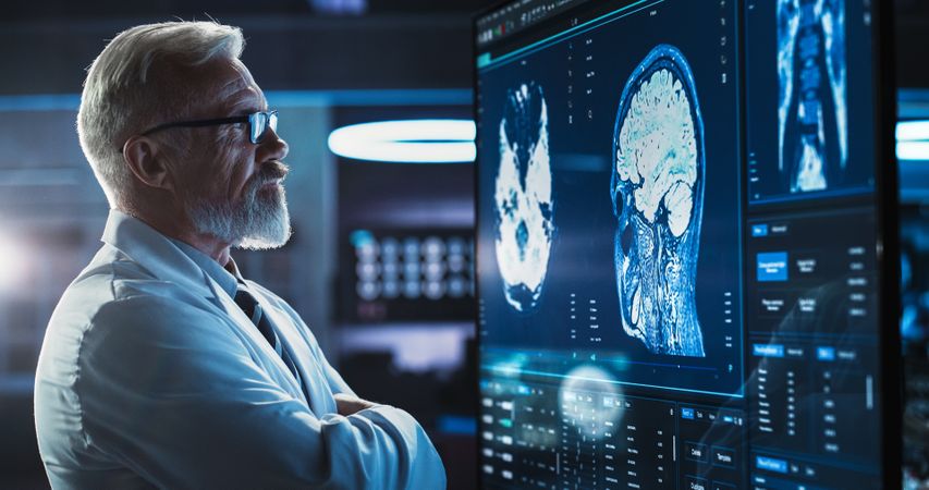 Neuroscientist, Neurosurgeon, Looks at TV Screen with Brain MRI Scan Images, Thinks about Sick Patient Treatment Method.