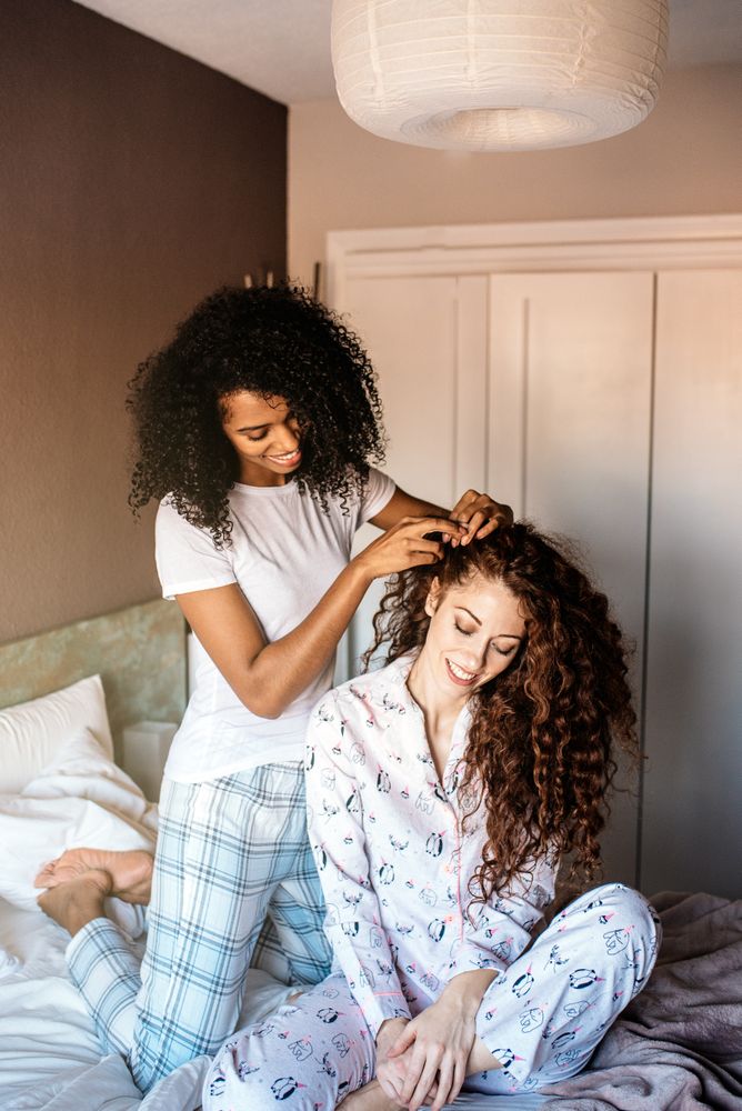 Woman combing another girl's hair in bed
