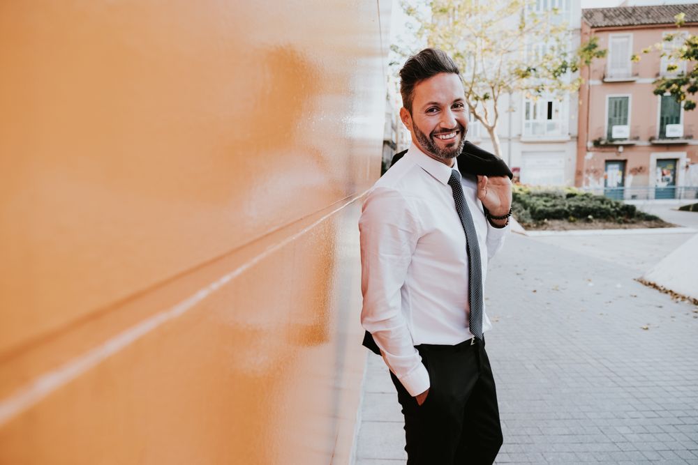 Adult smiling stylish man in costume near orange wall on street