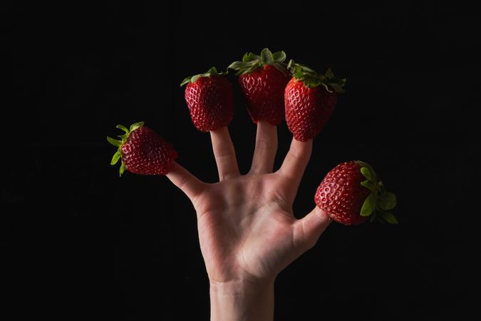 Hand of anonymous person wearing ripe strawberries on fingers