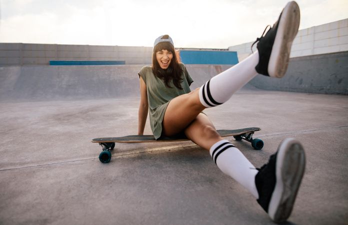 Female skateboarder sitting on a long board at skate park kicking out one leg