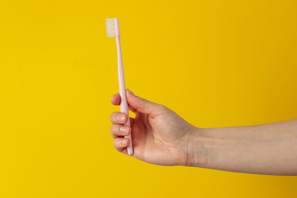 Female hand holds toothbrush on yellow background. Oral care