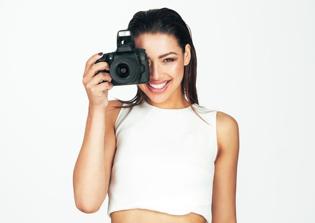 Woman in white top holding a dslr camera with one hand close to her face