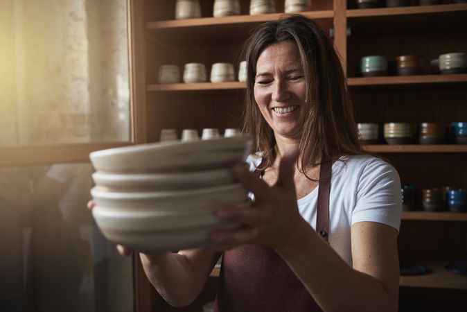 Smiling woman in leather apron inspecting a stack of handmade plates