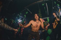 Sweaty long-haired shirtless male musician grabs microphone on stage during concert