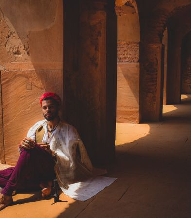 Man in traditional outfit sitting beside pillar