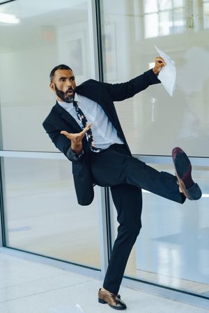 Nonchalant businessman in suit and tie throwing papers in the air in office