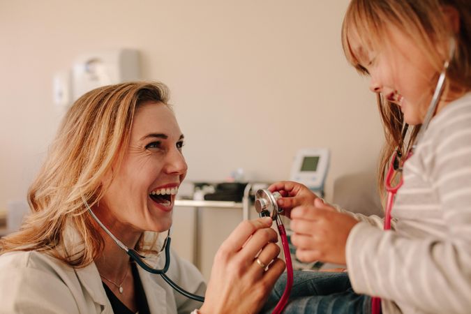 Female doctor and girl patient playing with stethoscope at the clinic