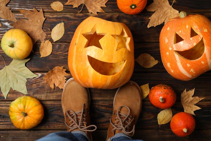Pumpkins, leaves and legs in boots on wooden background, top view