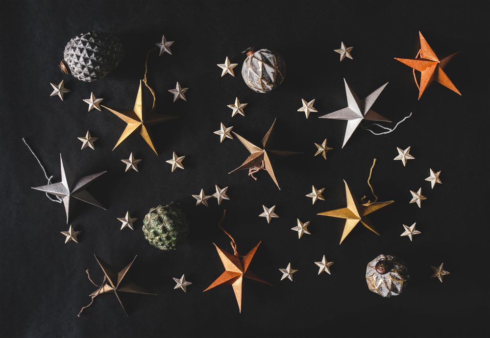 Flat-lay of colorful paper toy decorative stars, with pine cones and baubles